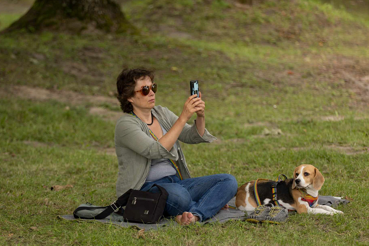 bohaterka artykułu siedząca na trawie ze swoim psem i robiąca zdjęcie komórką