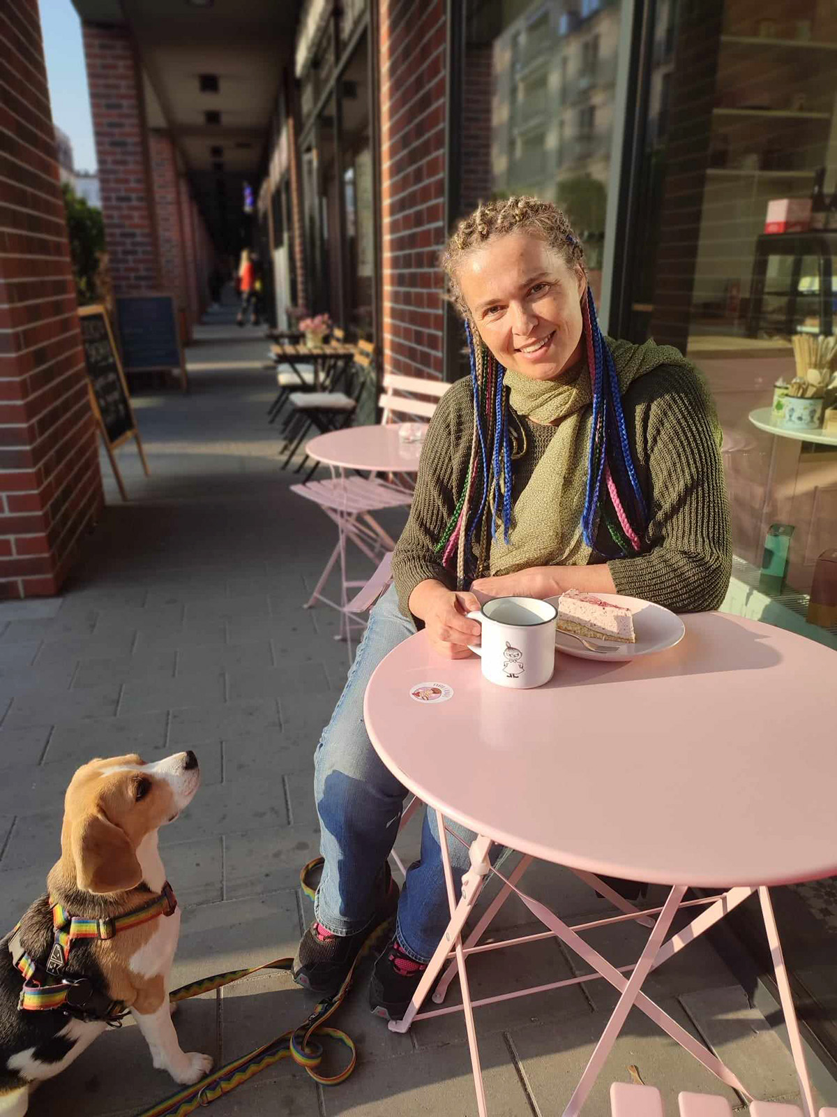 Barbara Sadurska przy stoliku kawiarnianym przed kawiarnią, patrzy na nią jej pies